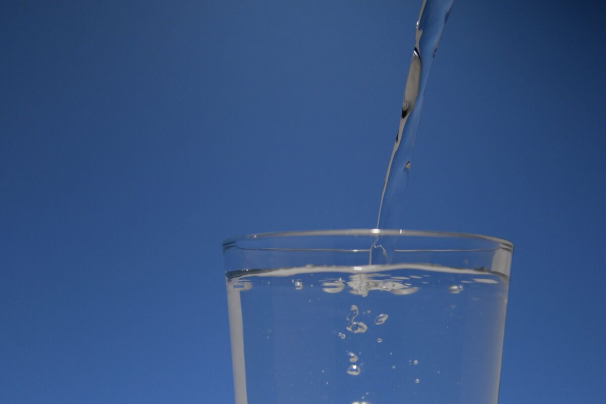 Clear filtered water pouring into a glass against a blue background